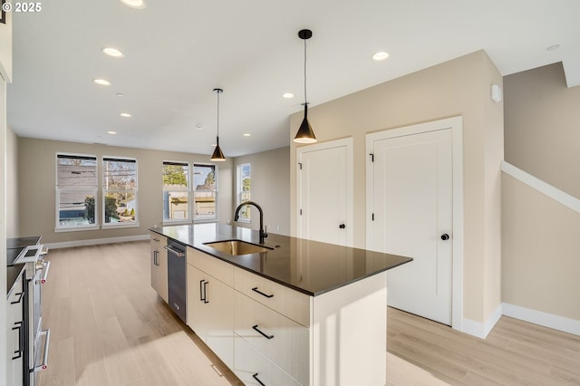 kitchen with light wood finished floors, dark countertops, a sink, and recessed lighting