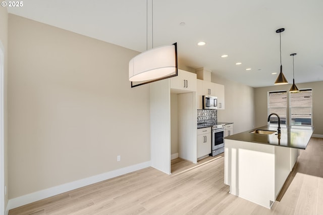 kitchen featuring white cabinets, a sink, stainless steel appliances, light wood-type flooring, and backsplash