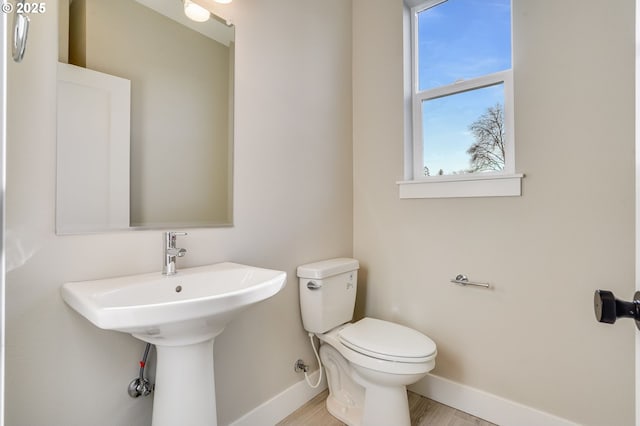 half bathroom with toilet, baseboards, and wood finished floors