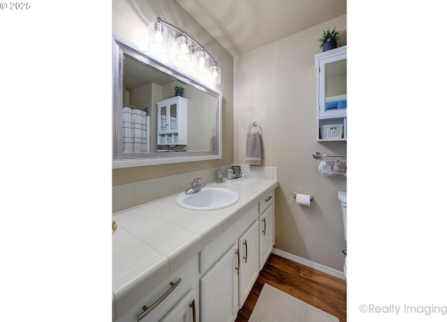 bathroom with vanity, toilet, wood finished floors, and baseboards