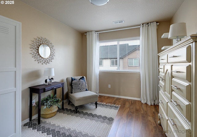 living area with visible vents, a textured ceiling, baseboards, and wood finished floors