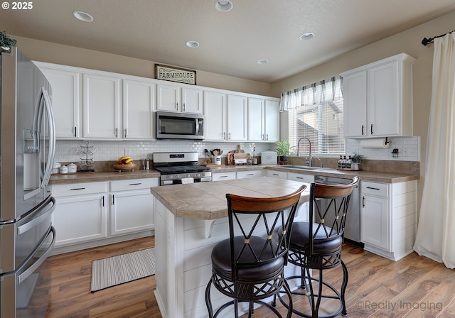 kitchen with a center island, light wood-type flooring, appliances with stainless steel finishes, a kitchen breakfast bar, and a sink