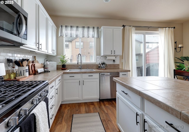 kitchen with a sink, stainless steel appliances, white cabinets, and tile countertops