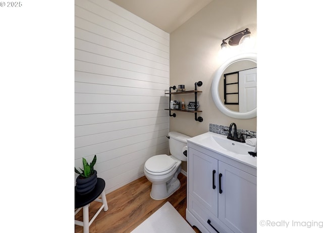 half bath with wood walls, toilet, vanity, and wood finished floors