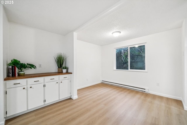 spare room featuring light wood-style floors, baseboards, a baseboard heating unit, and a textured ceiling