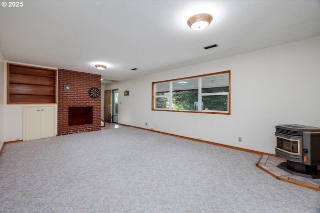 unfurnished living room with visible vents, a wood stove, carpet floors, a fireplace, and baseboards