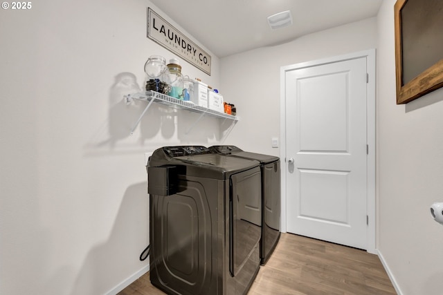 clothes washing area featuring laundry area, baseboards, wood finished floors, and washing machine and clothes dryer