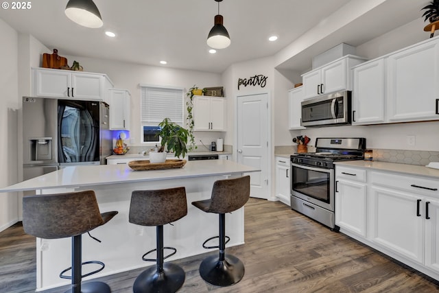 kitchen with stainless steel appliances, light countertops, white cabinetry, and pendant lighting