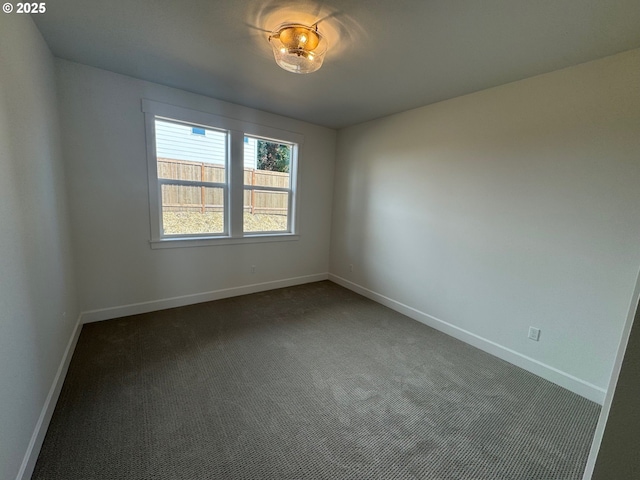empty room featuring baseboards and dark colored carpet