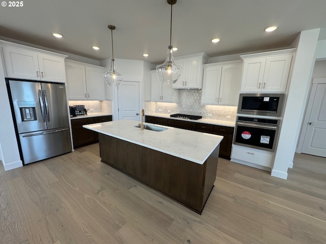 kitchen with light wood-style flooring, a sink, white cabinetry, backsplash, and appliances with stainless steel finishes
