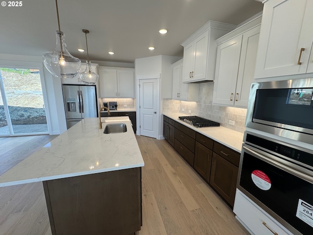 kitchen with a sink, light wood-style flooring, white cabinetry, and appliances with stainless steel finishes