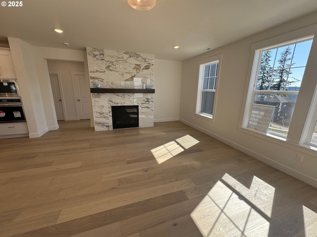 unfurnished living room with light wood-type flooring, baseboards, a premium fireplace, and recessed lighting