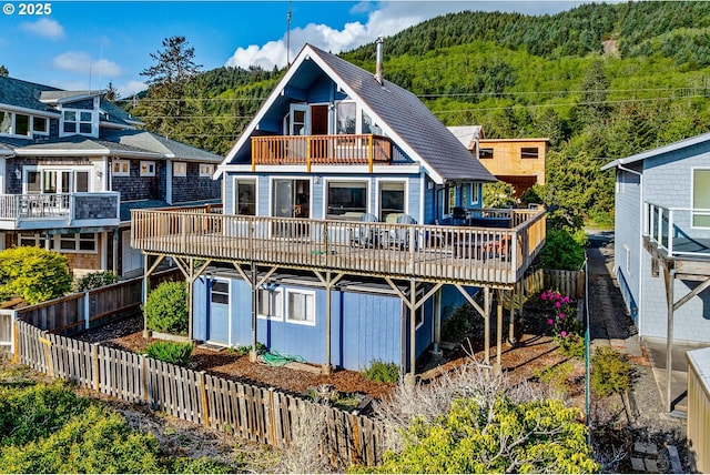 back of house featuring a view of trees, a balcony, a fenced backyard, and a wooden deck
