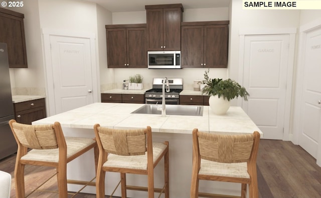 kitchen featuring dark brown cabinetry, appliances with stainless steel finishes, dark hardwood / wood-style flooring, and an island with sink