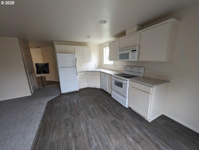 kitchen with white appliances, a sink, white cabinets, light countertops, and dark wood-style floors