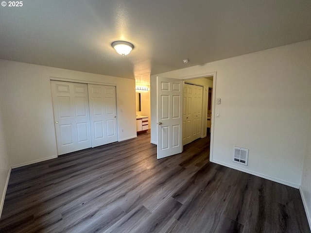 unfurnished bedroom featuring dark wood-style floors, baseboards, visible vents, and a closet