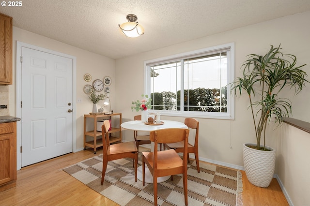 dining space featuring light wood-style floors, a textured ceiling, and baseboards