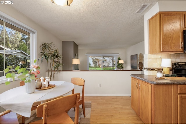 dining room with baseboards, a textured ceiling, visible vents, and light wood-style floors