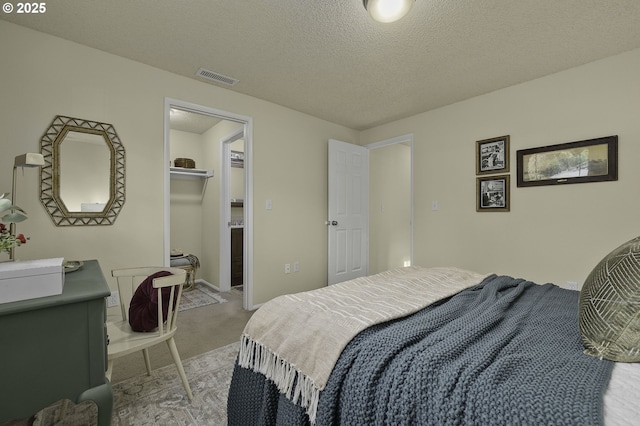 carpeted bedroom with a textured ceiling, a walk in closet, visible vents, and baseboards