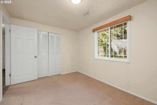 unfurnished bedroom featuring a textured ceiling, carpet flooring, visible vents, baseboards, and a closet