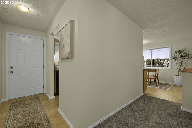 hall featuring light wood-type flooring, baseboards, visible vents, and a textured ceiling