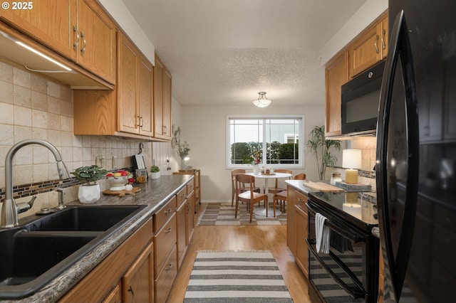 kitchen featuring a sink, light wood-type flooring, black appliances, brown cabinetry, and dark countertops