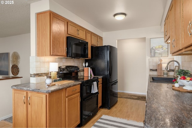 kitchen with dark countertops, black appliances, light wood-style floors, and a sink