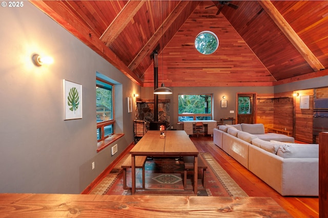 living room featuring beam ceiling, high vaulted ceiling, light hardwood / wood-style floors, wooden ceiling, and a wood stove