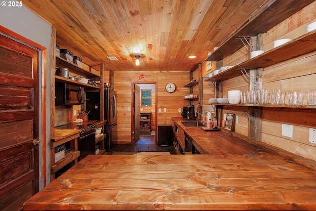 interior space with butcher block counters, sink, wood ceiling, wooden walls, and black appliances