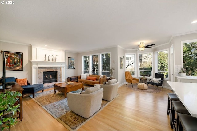 living area with baseboards, ornamental molding, light wood-style flooring, a fireplace, and a ceiling fan