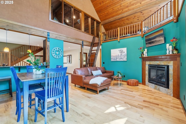 dining space featuring wood finished floors, high vaulted ceiling, wooden ceiling, a glass covered fireplace, and stairs