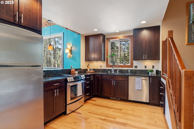 kitchen featuring a sink, dark stone counters, stainless steel appliances, and light wood-type flooring