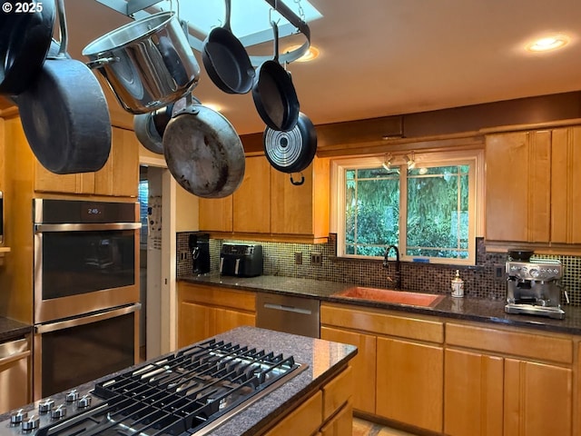 kitchen with a sink, dark stone counters, backsplash, and stainless steel appliances