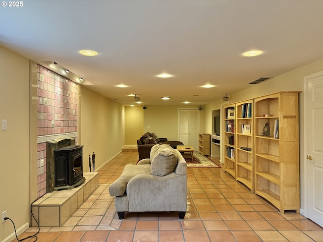 living area featuring light tile patterned floors, visible vents, baseboards, and a wood stove