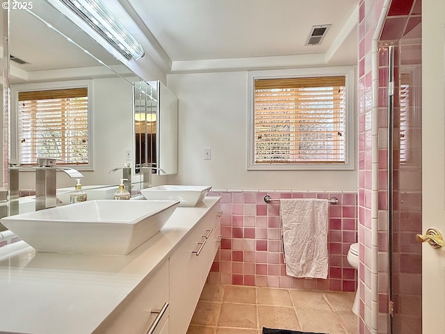 bathroom featuring a sink, a wainscoted wall, tile walls, and double vanity