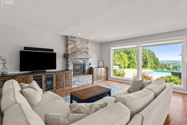 living area with recessed lighting, a textured ceiling, wood finished floors, and a stone fireplace