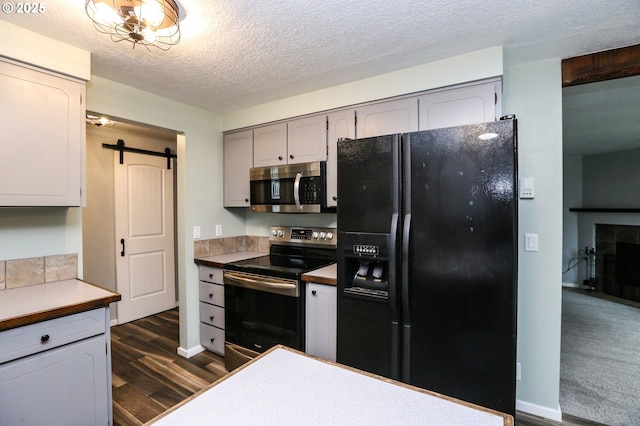 kitchen featuring gray cabinetry, dark wood-type flooring, a barn door, a textured ceiling, and appliances with stainless steel finishes