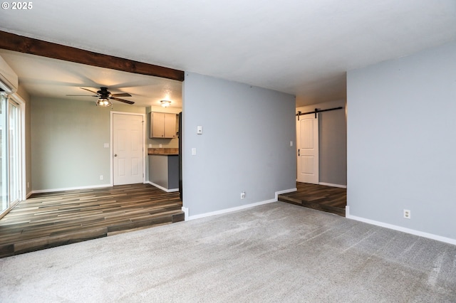 unfurnished living room with beam ceiling, a barn door, dark carpet, and ceiling fan