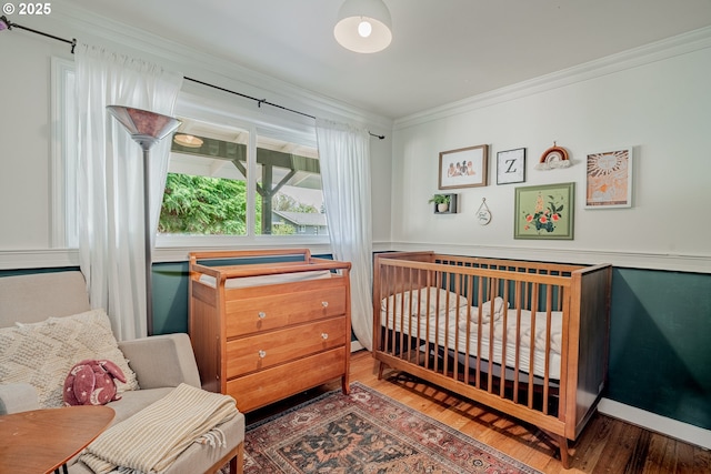 bedroom featuring crown molding, a crib, and wood finished floors