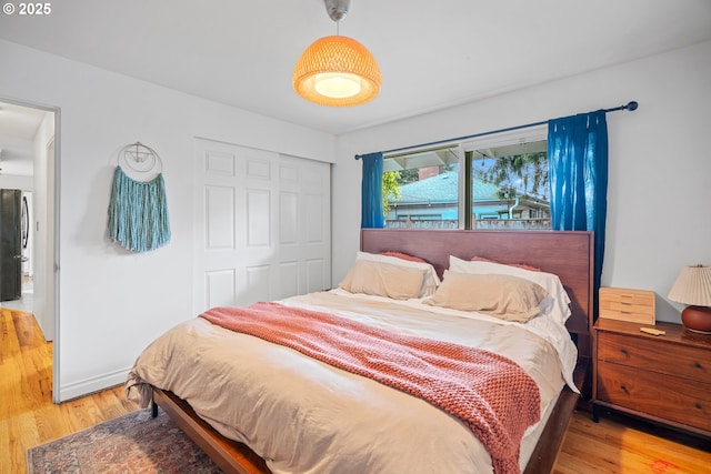 bedroom featuring freestanding refrigerator, baseboards, wood finished floors, and a closet