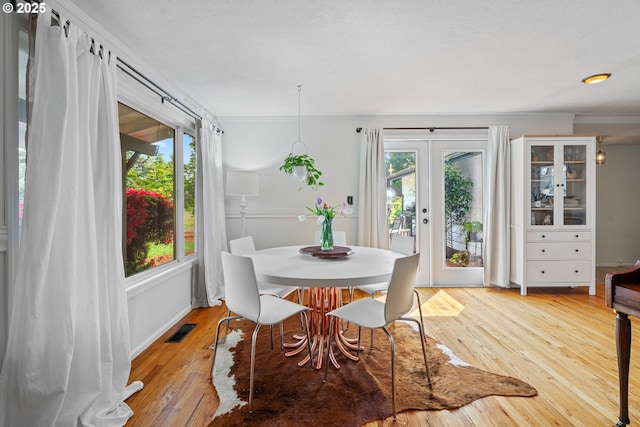 dining space with french doors, light wood finished floors, and visible vents
