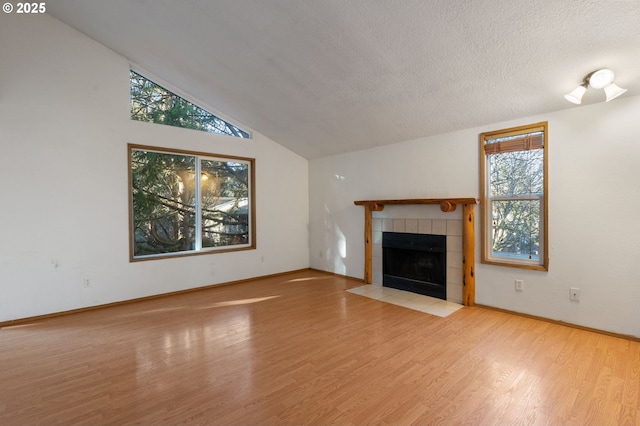 unfurnished living room featuring a tiled fireplace, vaulted ceiling, a wealth of natural light, and light hardwood / wood-style floors