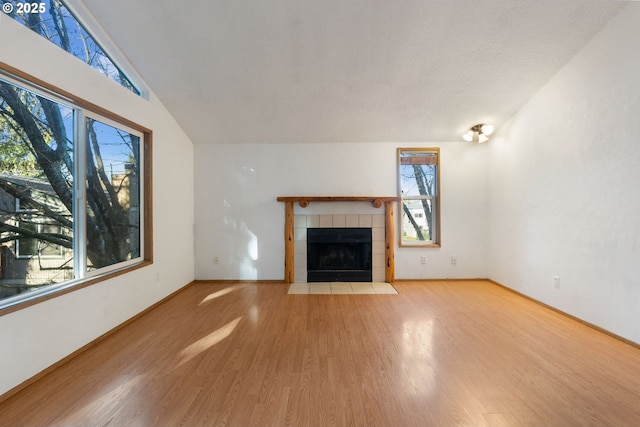 unfurnished living room with a tile fireplace, wood-type flooring, and lofted ceiling