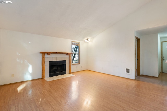 unfurnished living room featuring a tiled fireplace, vaulted ceiling, and light wood-type flooring