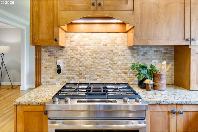 kitchen with backsplash, crown molding, wood finished floors, baseboards, and stainless steel gas range