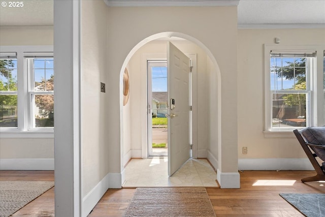 foyer with arched walkways, plenty of natural light, ornamental molding, and light wood finished floors