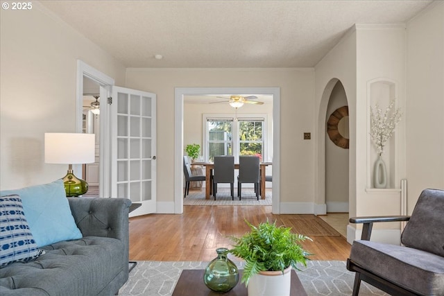 living room featuring baseboards, ceiling fan, crown molding, and wood finished floors