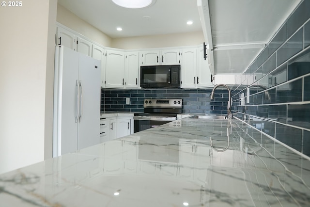 kitchen featuring light stone countertops, freestanding refrigerator, stainless steel range with electric stovetop, black microwave, and tasteful backsplash