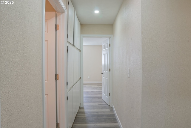 hallway featuring wood finished floors, baseboards, and a textured wall