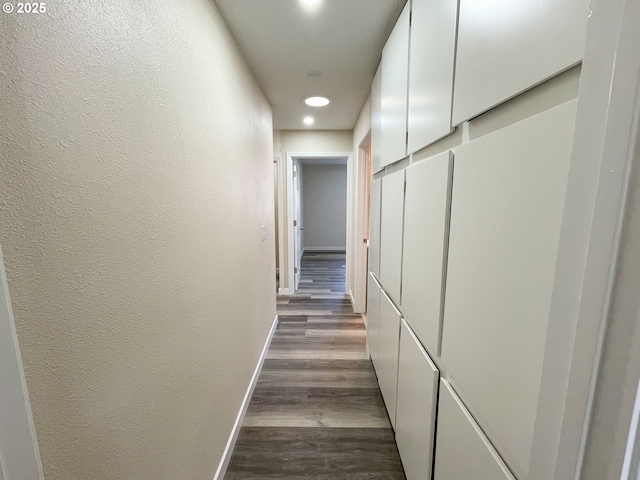 hall featuring dark wood-style floors, baseboards, and a textured wall